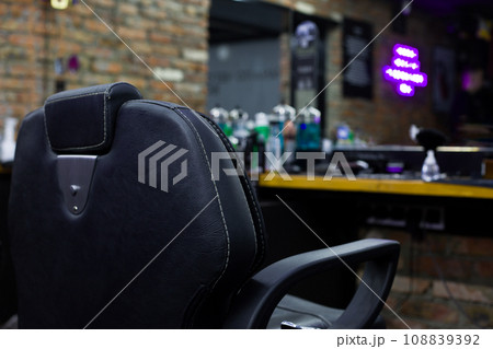 Back of a black leather chair with armrests in a barbershop in front of a mirror and a hairdresser's table with hair care tools 108839392