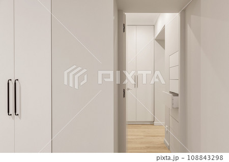 Minimalistic interior with white wooden cabinets, hidden chest of drawers and wooden flooring 108843298