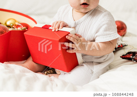 Close-up Adorable baby boy playing with Christmas baubles and new year gift. Winter holidays celebration and festive concept 108844248