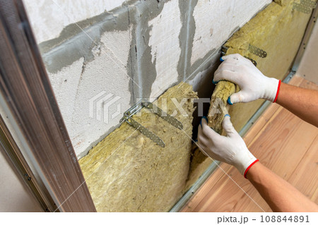 Worker insulating a room wall with mineral rock wool thermal insulation. Worker insulating a room wall with mineral rock wool thermal insulation. 108844891