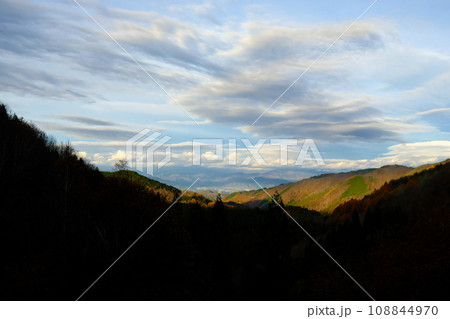 早朝に徐々に太陽に照らされる紅葉した山と雲 108844970