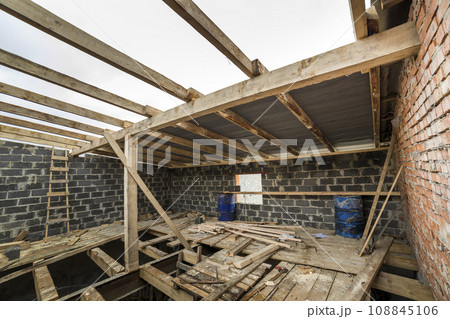 Two-storied building under construction and renovation. Perspective view of energy saving walls of large hollow foam insulation blocks and bricks, temporary wooden scaffolding, beams as roof frame. 108845106