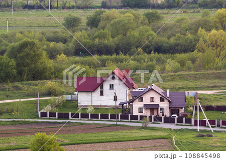 Quiet residential suburban area. Street with new modern comfortable brick cottages with yards and blooming gardens on background of beautiful green forest. Investments in real estate concept. Quiet residential suburban area. Street with new modern comfortable brick cottages with yards and blooming gardens on background of beautiful green forest. Investments in real estate concept. 108845498