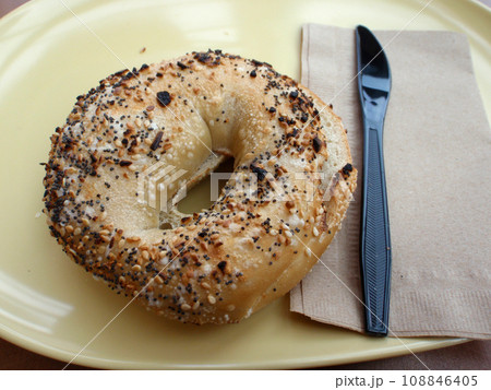 Everything Bagel and Plastic Knife on a yellow plate 108846405