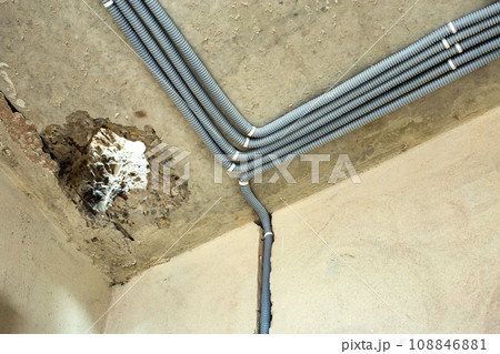 Electrical cables laid in protective corrugation installed on the ceiling and wall in a room under construction works. 108846881