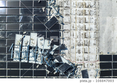 Consequences of natural disaster. Damaged by hurricane wind photovoltaic solar panels mounted on industrial building roof for producing green ecological electricity Consequences of natural disaster. Damaged by hurricane wind photovoltaic solar panels mounted on industrial building roof for producing green ecological electricity 108847003