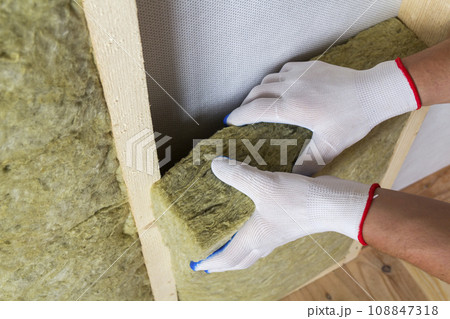 Close-up of worker hands in white gloves insulating rock wool insulation staff in wooden frame for future walls for cold barrier. Comfortable warm home, economy, construction and renovation concept. 108847318