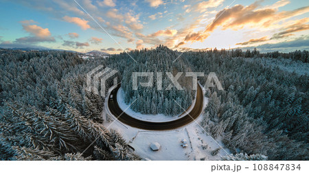 Aerial view of winter landscape with snow covered mountain hills and winding forest road in morning. 108847834
