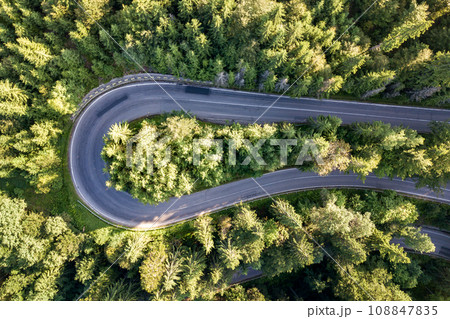 Aerial view of winding road in high mountain pass trough dense green pine woods. 108847835