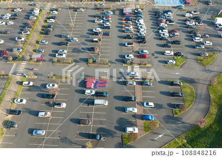 Aerial view of many colorful cars parked on parking lot with lines and markings for parking places and directions Aerial view of many colorful cars parked on parking lot with lines and markings for parking places and directions 108848216