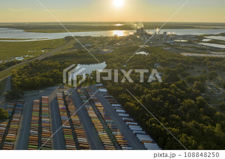 Aerial view of large cargo container yard with rows of freight containers and big factory manufacture structure. International shipment of produced goods concept 108848250