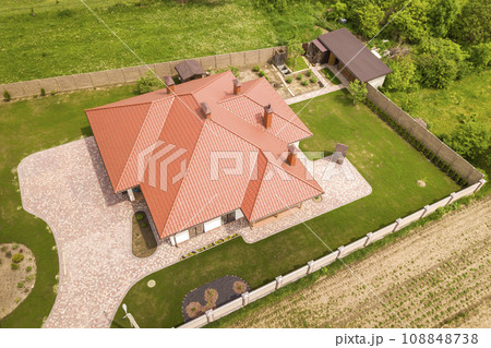 Aerial top view of new residential house cottage with shingle roof on fenced big yard on sunny day. 108848738