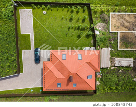 Aerial top view of house shingle roof with attic windows and black car on paved yard with green grass lawn. Aerial top view of house shingle roof with attic windows and black car on paved yard with green grass lawn. 108848742
