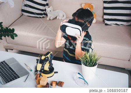Asian kid boy using VR glasses on robotic arm in workshop, Child learning programer control robot arm with sensors to pick up wood block, Technology education, Virtual Reality Simulator, industry 4.0 108850187