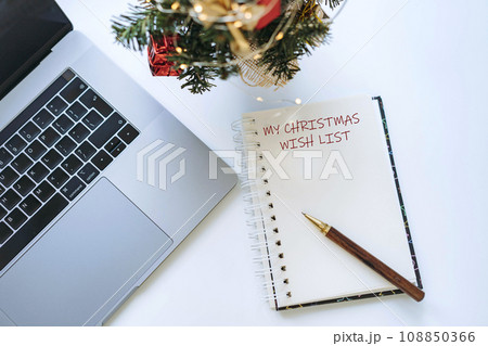 open notepad with wish list text. Laptop and decorated christmas tree nearby open notepad with wish list text. Laptop and decorated christmas tree nearby 108850366