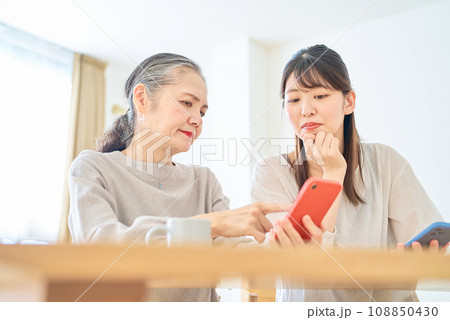 スマートフォンの画面を心配そうに見るシニア女性と若い女性 スマートフォンの画面を心配そうに見るシニア女性と若い女性 108850430