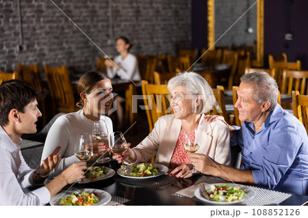 Young family and elderly couple of spouses eating in cafe celebrating event and communicating 108852126