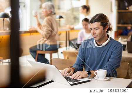 Concentrated designer working on laptop in cafe, drinking coffee 108852304