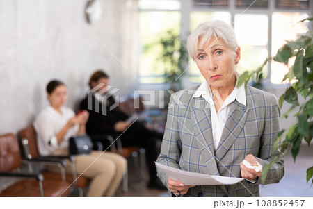 Upset aged female employee standing in office with papers 108852457