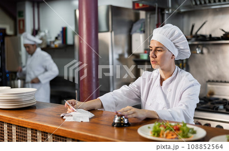 Female cook reads the paid check and presses the bell for the waiter in restaurant Female cook reads the paid check and presses the bell for the waiter in restaurant 108852564