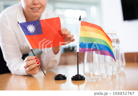 Female hands placing Taiwanese and rainbow flags on negotiating table 108852767