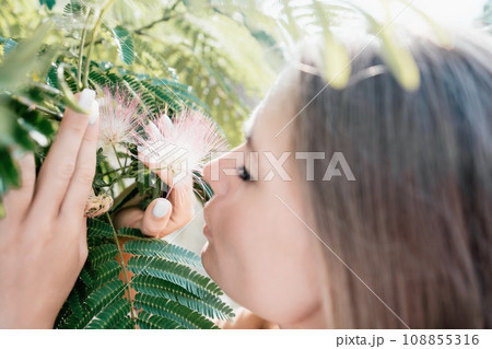 Beauty portrait of happy woman closeup. Young girl smelling Chinese acacia pink blossoming flowers. Portrait of young woman in blooming spring, summer garden. Romantic vibe. Female and nature Beauty portrait of happy woman closeup. Young girl smelling Chinese acacia pink blossoming flowers. Portrait of young woman in blooming spring, summer garden. Romantic vibe. Female and nature 108855316
