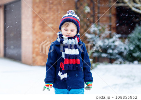 Cute little funny child in colorful winter fashion clothes having fun and playing with snow, outdoors during snowfall. Active outdoors leisure with children. Kid boy and toddler catching snowflakes. 108855952