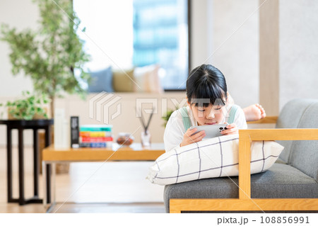 リビングでスマホで遊ぶ小学生の女の子。 108856991