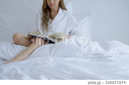 Young woman reading book on bed at home. Young woman reading book on bed at home. 108857874