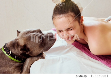 Woman squints and laughs when dog licks her face while standing next to her bed. Woman squints and laughs when dog licks her face while standing next to her bed. 108860061
