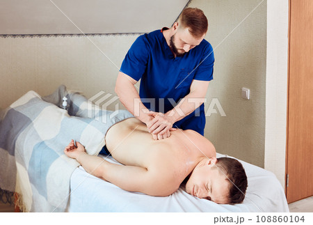 Trained mobile masseur massages muscles of young European man, deep tissue massage for back pain. Trained mobile masseur massages muscles of young European man, deep tissue massage for back pain. 108860104