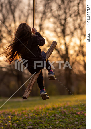 Unrecognizable girl swings on homemade swing in nature, in park, in village, in children's camp. Child protection. Unrecognizable girl swings on homemade swing in nature, in park, in village, in children's camp. Child protection. 108862583