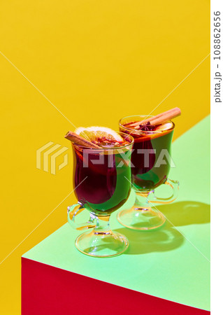 Glasses with delicious red mulled wine with oranges and cinnamon against colorful background. Traditional hot drink in winter season. Poster 108862656