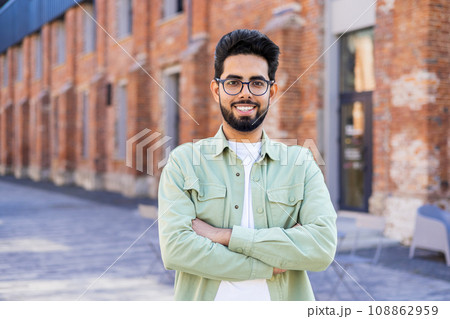 Portrait of young man in casual clothes joyful businessman smiling and looking at camera with arms crossed, Indian man outside office building. Portrait of young man in casual clothes joyful businessman smiling and looking at camera with arms crossed, Indian man outside office building. 108862959