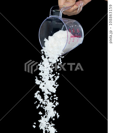 Salt fall, crystal white grain peanuts explode abstract cloud fly from measuring cup. Beautiful complete seed salt, food object design. Selective focus freeze shot black background isolated 108863159