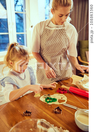 Woman, mother cooking Christmas cooking with her little daughter in modern kitchen in the evening. Following traditions Woman, mother cooking Christmas cooking with her little daughter in modern kitchen in the evening. Following traditions 108863360