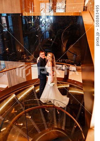 Bride and groom embracing on a golden spiral staircase. Bride and groom embracing on a golden spiral staircase. 108863495