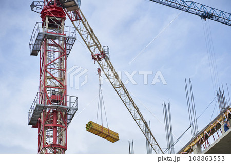 A construction crane on the background of a skyscraper under construction and a blue sky. Construction of new buildings using a crane. Tower crane. High quality photo A construction crane on the background of a skyscraper under construction and a blue sky. Construction of new buildings using a crane. Tower crane. High quality photo 108863553