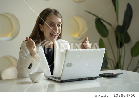 Happy excited woman at home workstation triumphing with raised hands 108864750
