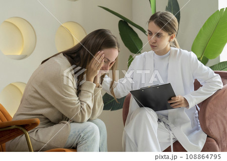 Worried young patient sits at a psychologist's appointment and talks about mental problems, an attentive female doctor listens and makes notes 108864795