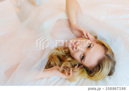 Morning of the bride. Delicate and beautiful blonde bride in bed under veil. 108867198