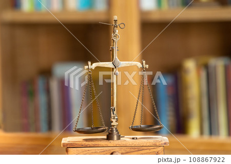 Close up to Golden vintage Scale Symbolic of Legal and Law section is standing on wood base in front of Library shelf. Close up to Golden vintage Scale Symbolic of Legal and Law section is standing on wood base in front of Library shelf. 108867922