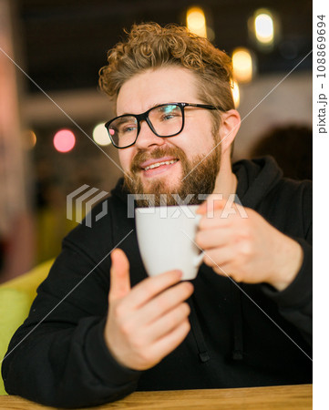 Portrait Bearded curly man smiling confident drinking coffee in restaurant or coffee shop. Millennial generation and Gen Y 108869694