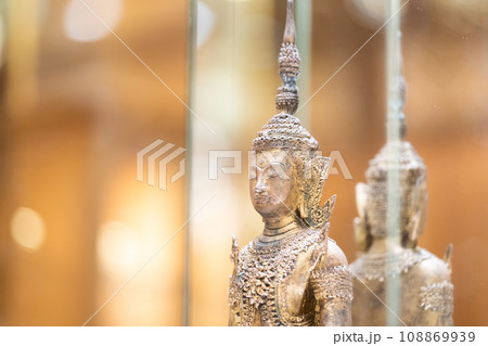Deity statue standing straight made of brass, wearing gold costume with Chada on top of his head in a luxury wood mirror closet. 108869939