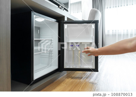 Man Hand opened mini small refrigerator and reached drinking plastic water bottle under the wood counter in the hotel resort bedroom. Man Hand opened mini small refrigerator and reached drinking plastic water bottle under the wood counter in the hotel resort bedroom. 108870013