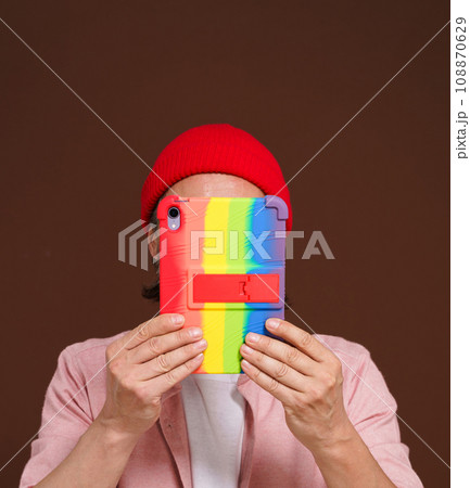 Anonymous person conceals face over tablet PC with LGBT gay rainbow colors. Intersection of digital identity and LGBTQ pride, emphasizing need for privacy and protection in digital space of gay pride Anonymous person conceals face over tablet PC with LGBT gay rainbow colors. Intersection of digital identity and LGBTQ pride, emphasizing need for privacy and protection in digital space of gay pride 108870629