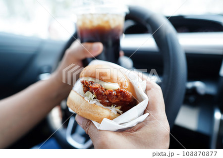 Asian woman driver hold and eat hamburger in car, dangerous and risk an accident. Asian woman driver hold and eat hamburger in car, dangerous and risk an accident. 108870877