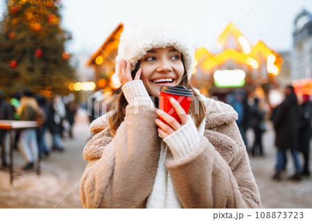 Young woman in winter style clothes posing at festive street market. Woman enjoying winter moments. 108873723