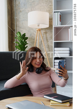 Happy girl checking social media holding smartphone sitting at sofa in living room at home. relaxing concepts Happy girl checking social media holding smartphone sitting at sofa in living room at home. relaxing concepts 108875788