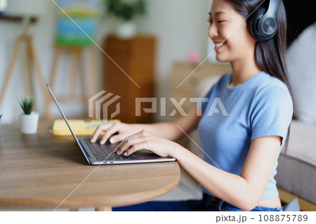 woman wearing headphones on comfortable couch listening to using computer laptop and music 108875789